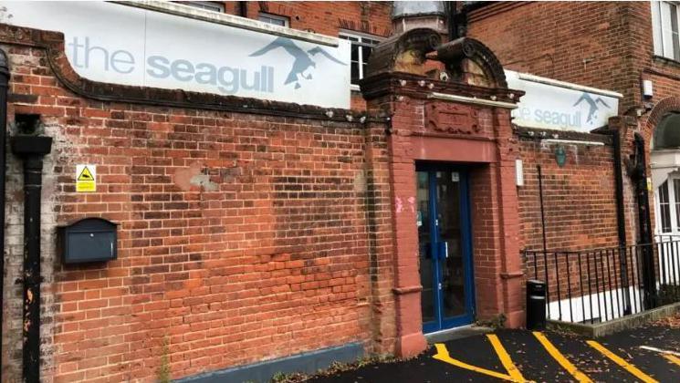 A red brick theatre with blue doors and white and blue sign above with "The Seagull" written on it.