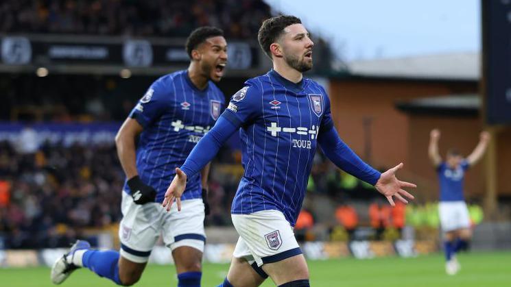 Conor Chaplin in a blue Ipswich Town shirt runs away to celebrate a goal being scored