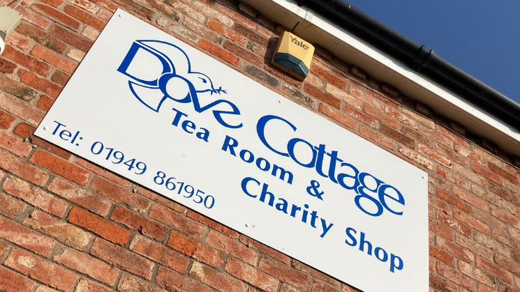 Sign of Dove Cottage tea room and charity shop with phone number on a wall 