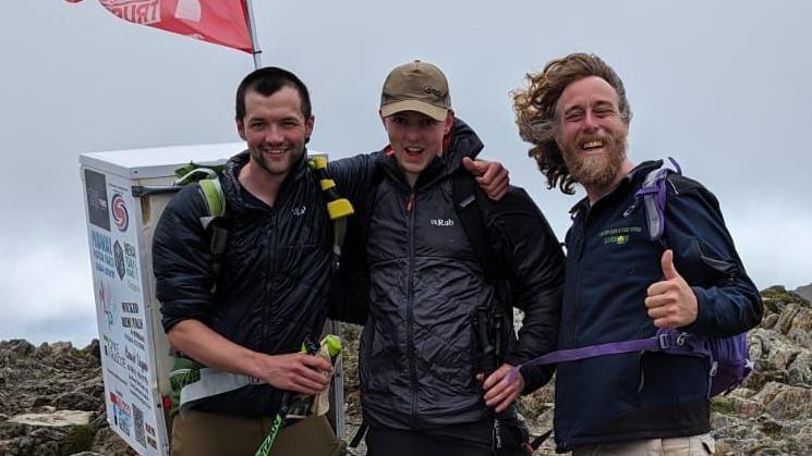 Three men, one with a fridge on his back, up Snowdonia