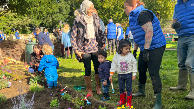 Small children in wellies and some parents in a garden, planting trees