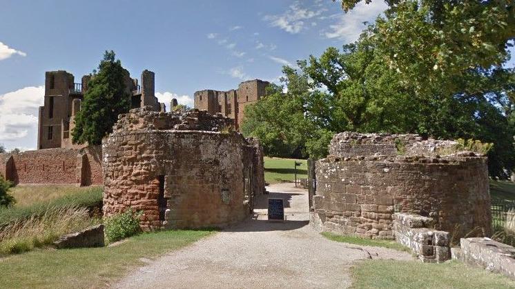 Several stone ruins leading up to the ruins of a castle, with paths in between them and some green trees to one side.
