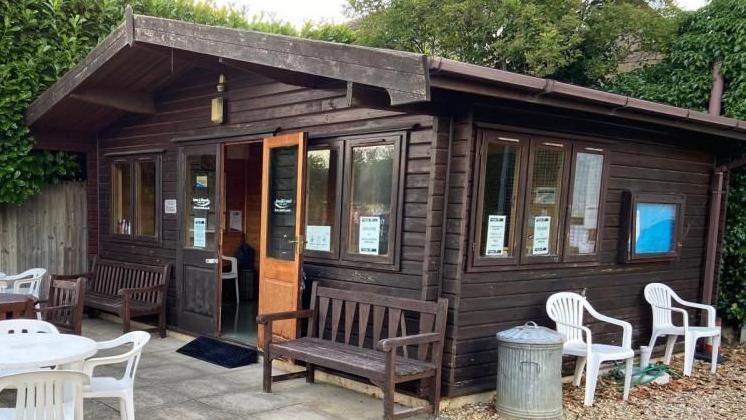 A polling station at Castor and Ailsworth Tennis Club, showing a brown chalet style shed, with chairs outside