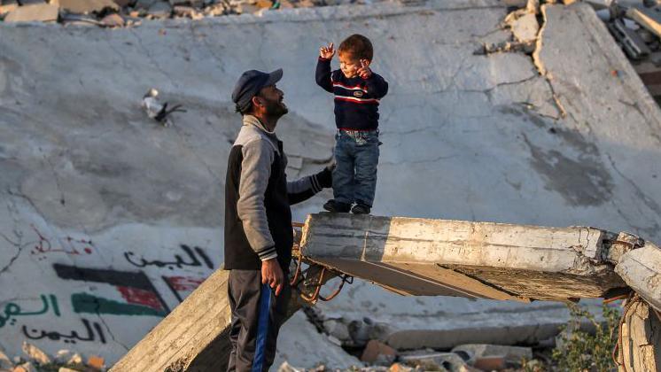 A man speaks with a boy standing on a broken concrete beam by the rubble of a collapsed building at a camp for people displaced by conflict in Bureij in the central Gaza.