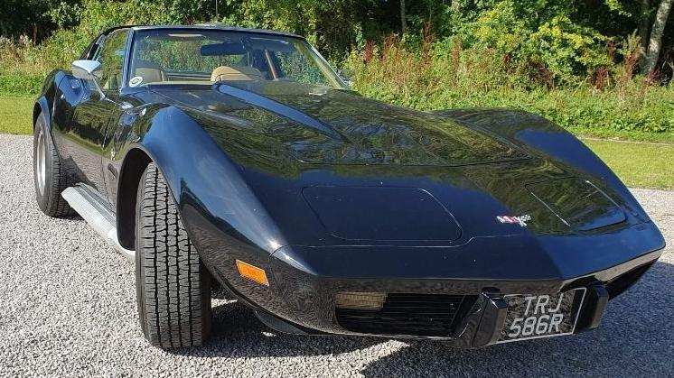 A black corvette T-top parked on a gravel driveway.