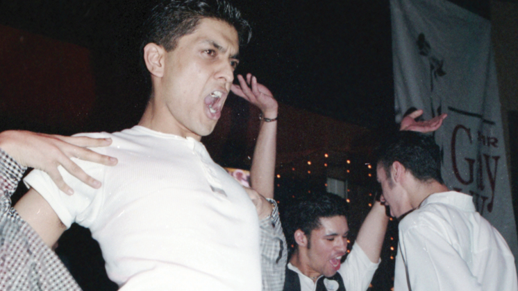 Three people dancing. The person in the foreground is wearing a white t shirt. The two in the background are wearing white shirts.