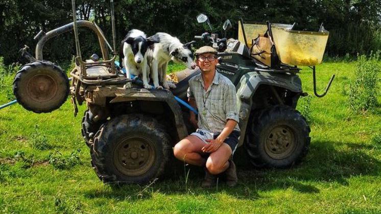 Karl Franklin smiling for the camera with his dogs next to a tractor on a sunny day.