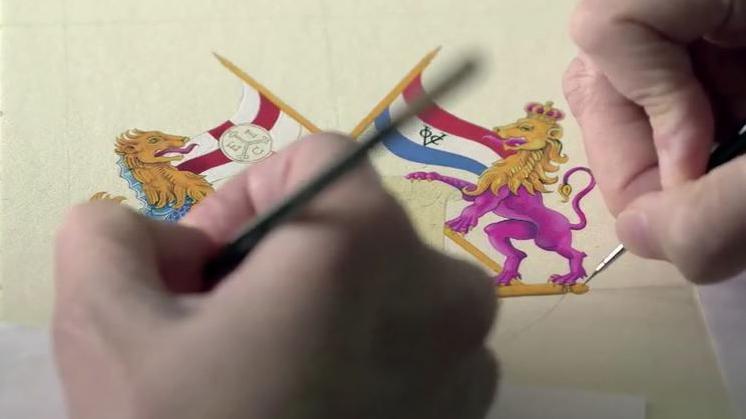 An intricate painting of small gold, pink and blue lion statues, holding flags - with two hands painting them.