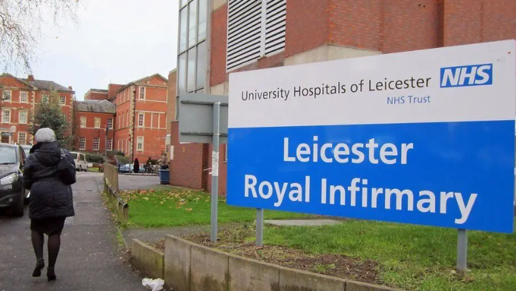 A sign outside the Leicester Royal infirmary with a person walking by in the background