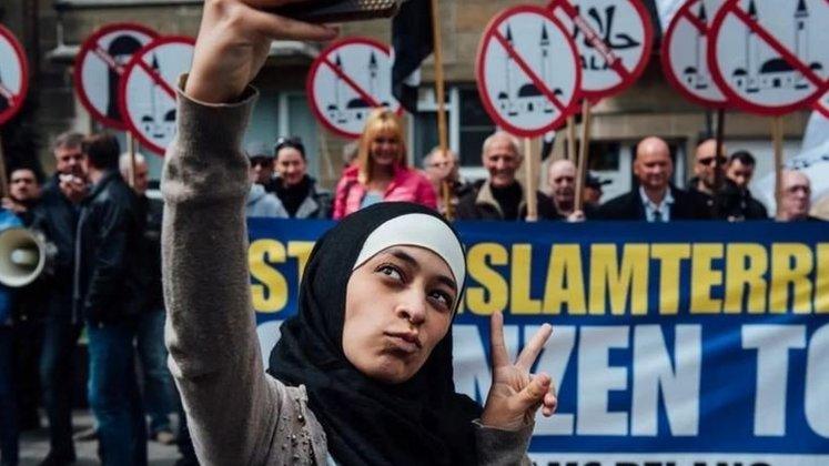 Photo of Zakia Belkhiri taking a selfie with Vlaams Belang protesters in the background