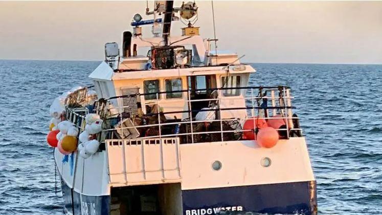 A fishing boat, with Bridgwater written on the back and its decks filled with crabbing pots, bobs on the sea 