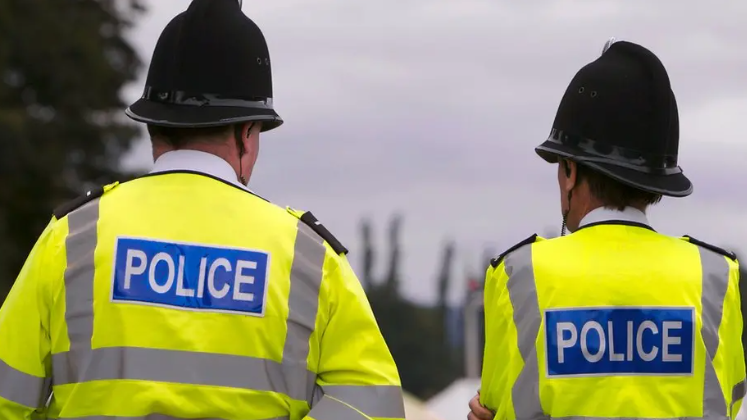 Two police officers with their backs to the camera. They are wearing high-vis jackets and black police helmets 