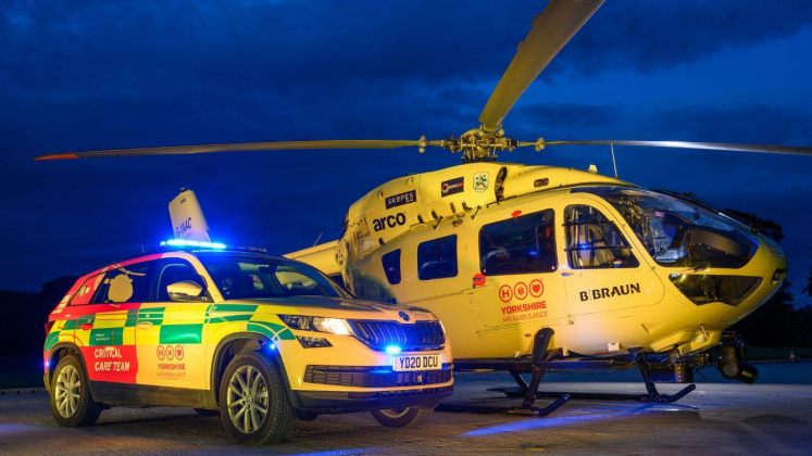 One of the yellow Yorkshire Air Ambulances, next to an ambulance car, taken at night.