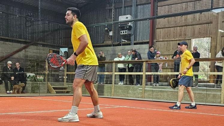 Two men in yellow T-Shirts on a what looks like a clay padel court