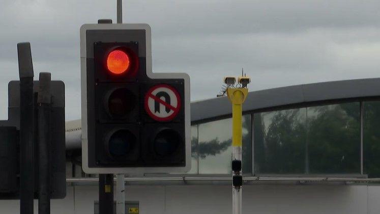 A red light on a set of traffic lights, with yellow speed cameras placed next to them