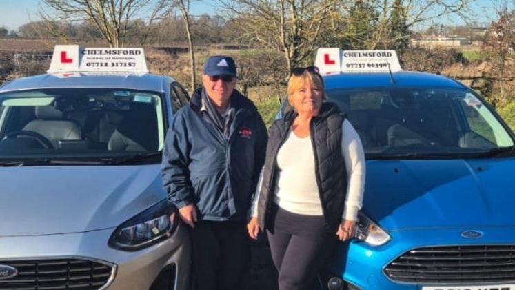 A man and a woman standing next to driving instructor cars