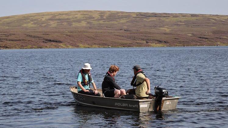 A small boat with three men on board carrying a conservation survey on a large loch with hillside in the background
