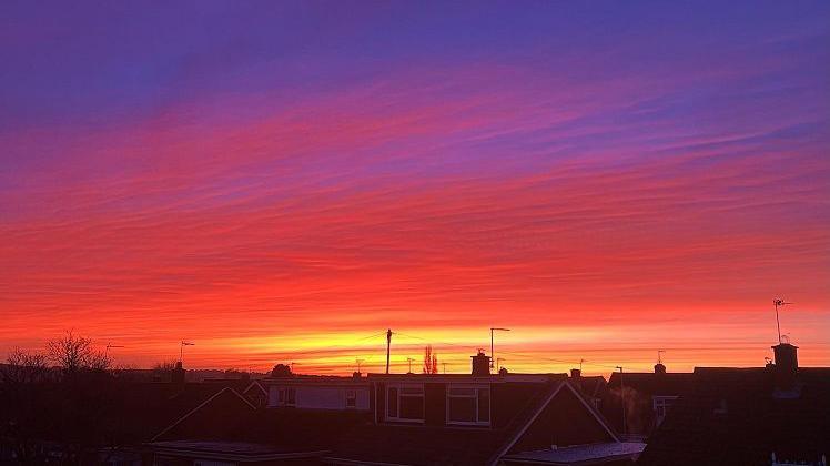 A mostly red sky with yellow stripes can be seen above the roofs of homes in Stone.