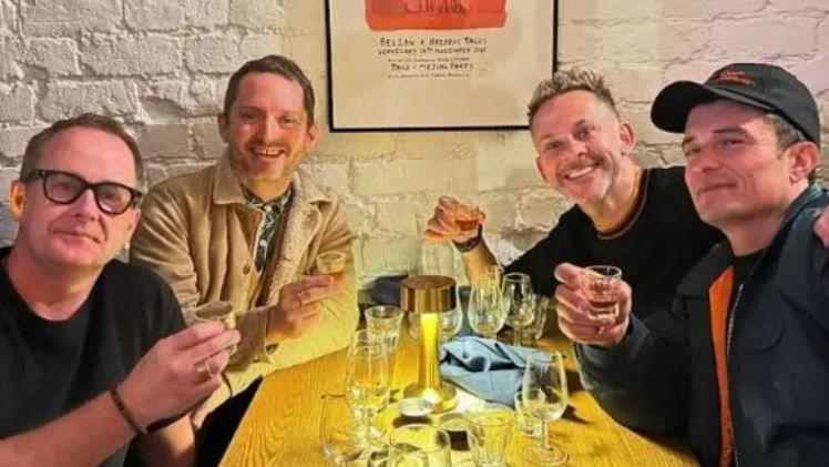 (L-R) Billy Boyd, Elijah Wood, Dominic Monaghan and Orlando Bloom sit around a table in a restaurant, holding shot glasses 