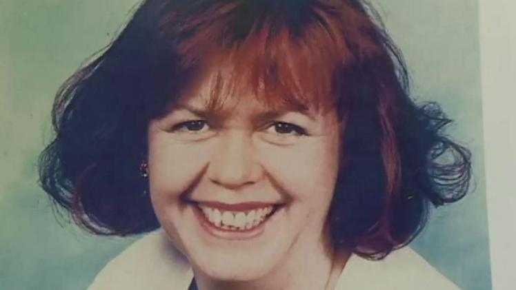 A woman with brown-red shoulder-length hair smiles into the camera. 