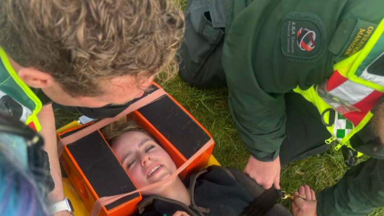 A woman on a stretcher in a neck brace is tended to by a paramedic
