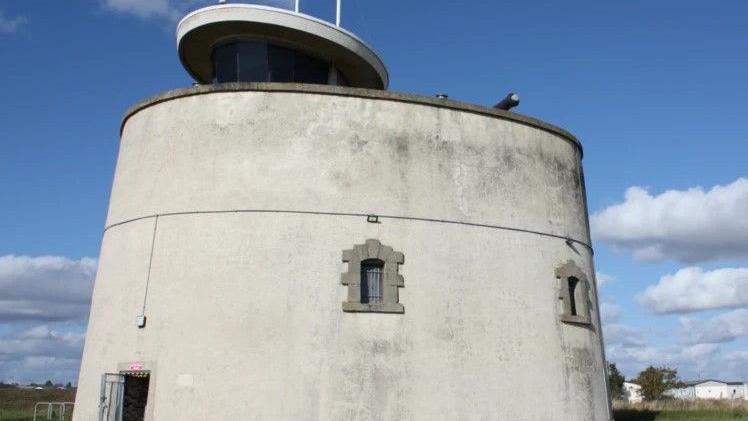 The round, grey exterior of Jaywick Martello Tower featuring small windows reinforced with bricks 