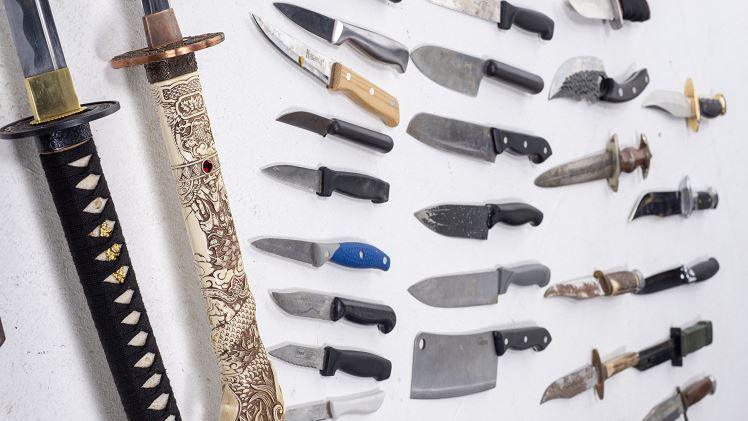 A selection of knives of all shapes and sizes, from machetes, to kitchen knives to longer knives in covers.