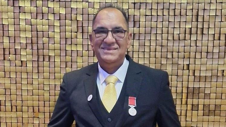 Moez wearing a grey suit and a yellow tie. He is balding and wears black-framed glasses. He is smiling.