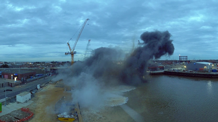 Smoke over the River Yare in the aftermath of a bomb blast, with a yellow crane visible behind it 