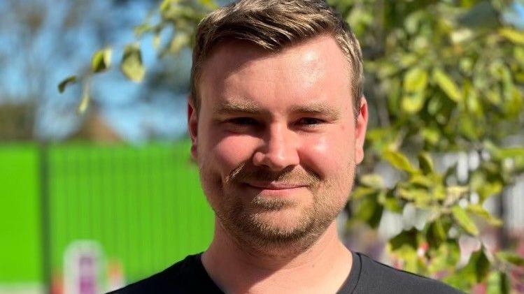 Dan King has short brown hair and a brown goatee. He smiles at the camera and is wearing a black t-shirt