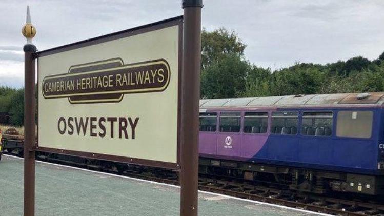 A brown and beige Cambrian Heritage Railways platform sign at Oswestry station