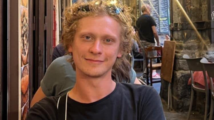 Syeva Bondarenko with curly blonde hair sits in a restaurant. He is wearing sunglasses on his head and a black top.