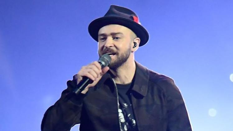 Justin Timberlake performing on stage. He is wearing a black hat, jacket and trousers.