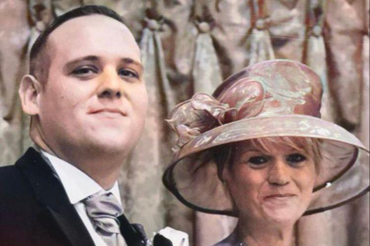 The picture shows a man and woman looking at the camera. The man on the left has short brown hair and is wearing a suit and tie. The woman on the right has short blonde hair and is wearing a large pink hat. They are dressed in what appear to be wedding clothes.