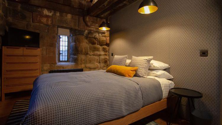 A bedroom inside the Cook Street Gate luxury flat showing a nicely made double bed, bedroom furniture and a window