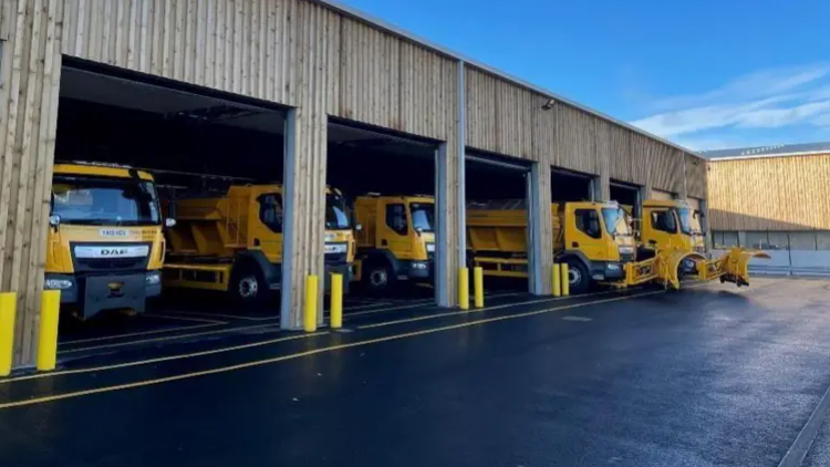 A view of Warminster salt depot with five yellow gritting vehicles parked at a holding station
