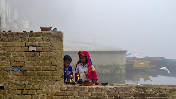 Boys light lamps on a brick wall on a bank of the river Yamuna in Delhi. Smog engulfs their surroundings