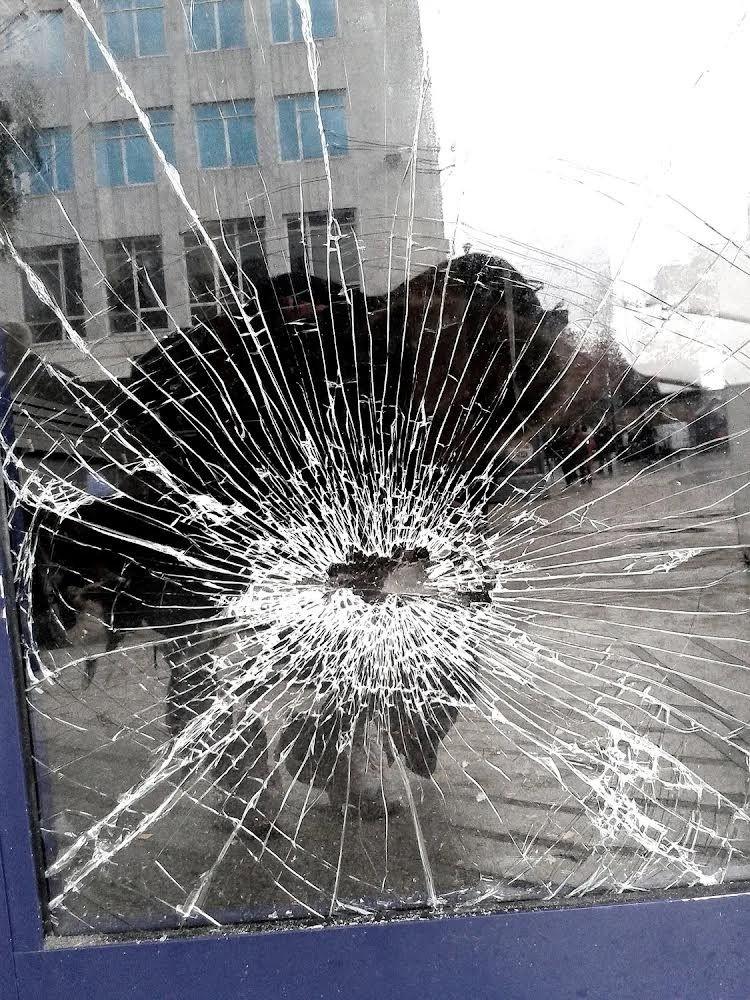 A reflection of a photographer taking a picture of broken glass in a door window.