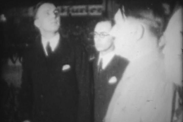 A sideways view of Hitler nearest to the camera, with Gareth Jones standing to his right. Gareth is in a black suit with a black tie and white shirt. It is a grainy, blurred black and white image.