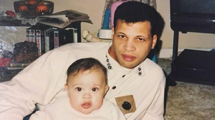 Antonio lies on the floor next to Ashley who is a baby, both looking toward the camera. The photo has a nostalgic, family feel, likely taken in the 1990s