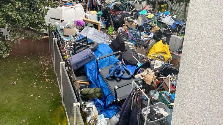 A view from the first floor window overlooking a garden piled high with rubbish and junk