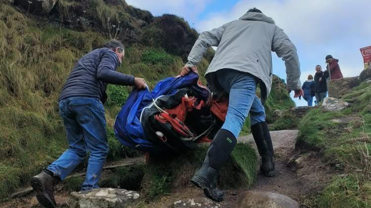 Volunteers carrying some of the life raft up a steep, rocky path.