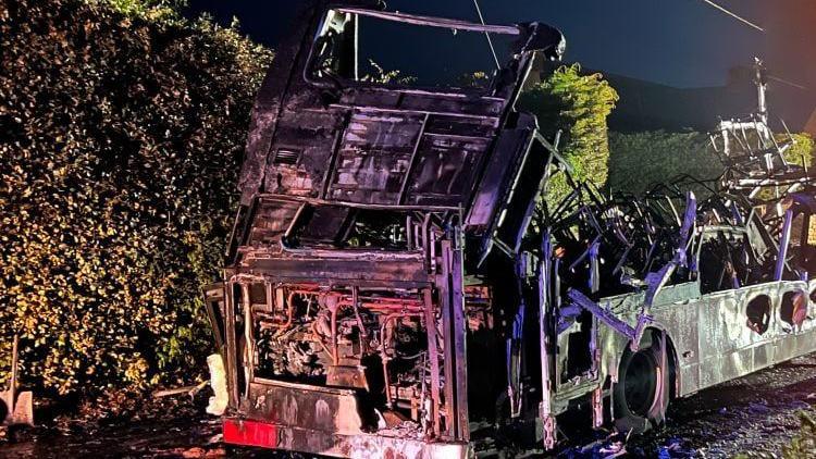 A night time photograph of the burnt-out carcass of the bus