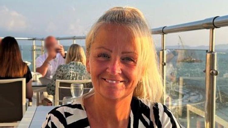 Anita Rose is pictured in a roof top dining establishment, smiling with her blonde hair tied back. She is wearing a black and white top.