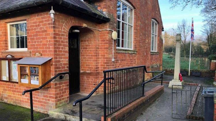 The outside of Scaleby Hall, which is a red brick building. A ramp and steps lead up to the black door.