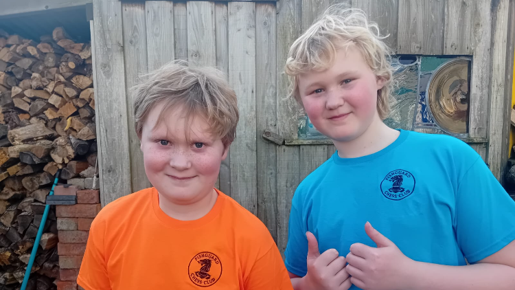 Llun yn dangos dau fachgen ifanc yn gwenu at y camera mewn crysau t oren a glas.