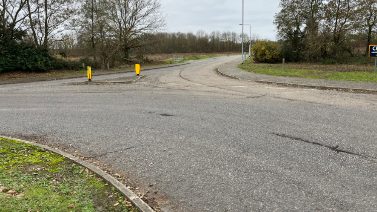 A roundabout with neon bollards in the centre. There is green patches of grass either side and a field can be seen in the distance. 