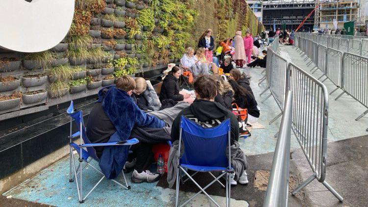 People sit in he queue on camping chairs