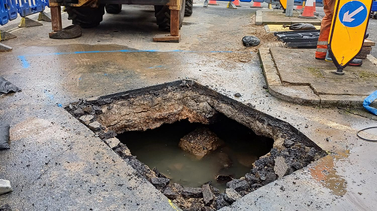 Large hole in road, filled with water. 