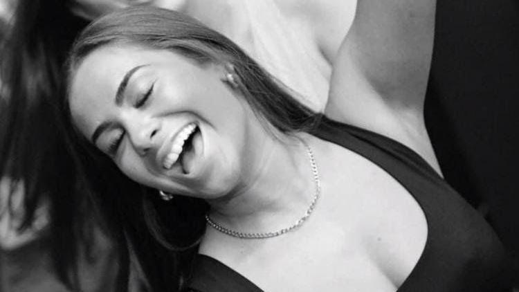 A woman smiling with her eyes closed and arms raised in a black and white photograph